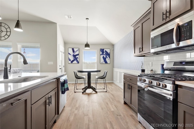 kitchen featuring light wood-style flooring, stainless steel appliances, a sink, light countertops, and tasteful backsplash