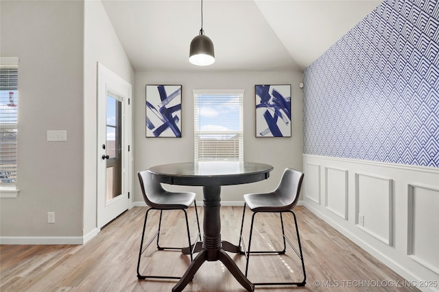 dining area featuring lofted ceiling, light wood-style floors, a decorative wall, and wainscoting