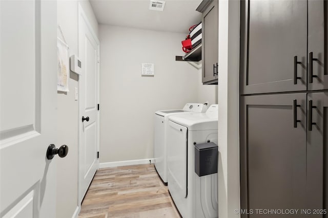 laundry area with cabinet space, light wood finished floors, baseboards, visible vents, and washing machine and clothes dryer