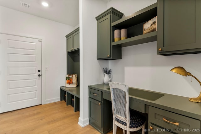 home office featuring light wood finished floors, built in desk, and visible vents