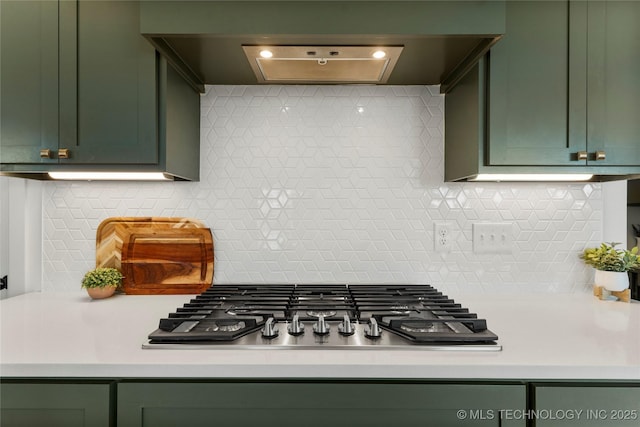 kitchen featuring stainless steel gas cooktop, green cabinets, ventilation hood, decorative backsplash, and light countertops