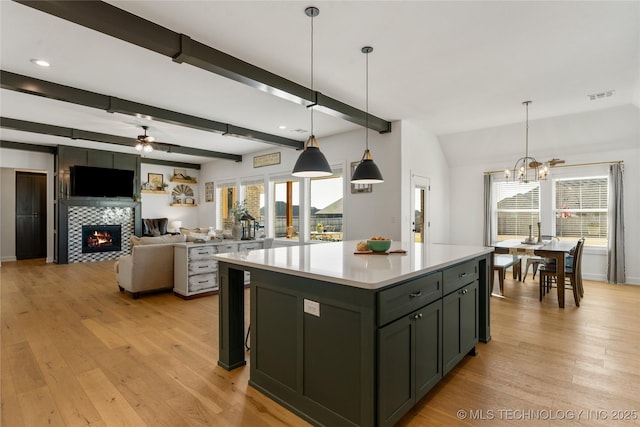 kitchen with visible vents, ceiling fan with notable chandelier, a kitchen island, light countertops, and light wood-type flooring