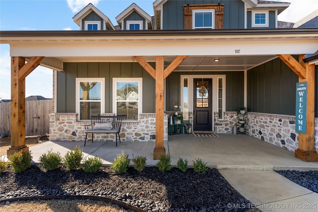 doorway to property featuring stone siding, fence, a porch, and board and batten siding