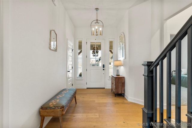 entryway featuring light wood-style floors, stairs, baseboards, and a notable chandelier