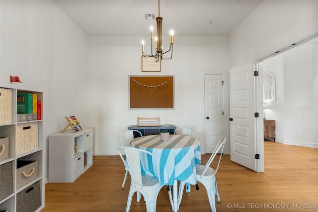 dining area with visible vents, baseboards, light wood-style flooring, and an inviting chandelier