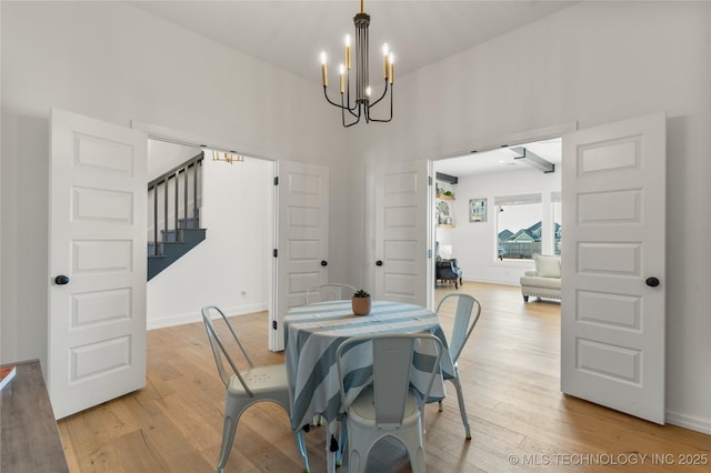 dining space featuring stairs, a notable chandelier, light wood-type flooring, and a towering ceiling