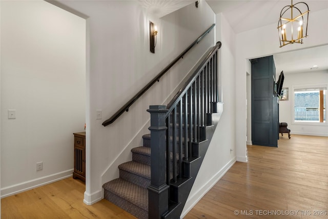 staircase with an inviting chandelier, baseboards, and wood finished floors