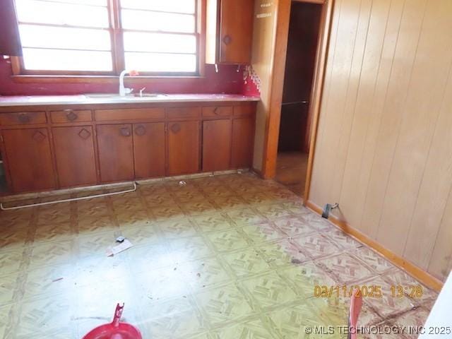 kitchen featuring wooden walls, light floors, brown cabinets, and a sink