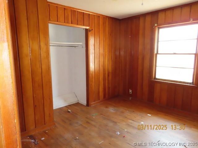 unfurnished bedroom featuring multiple windows, wood finished floors, and wood walls