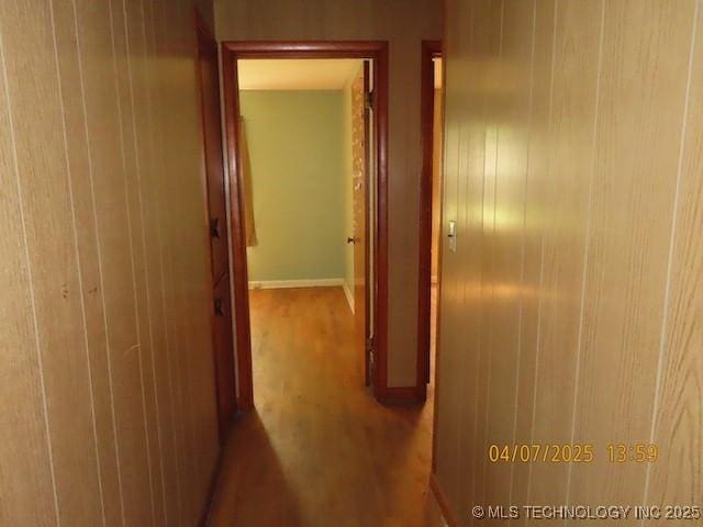 hallway featuring baseboards, wood walls, and wood finished floors