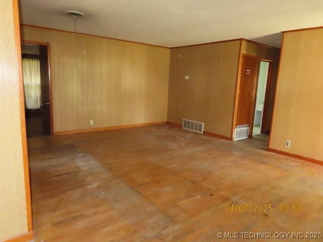 spare room with wood walls, baseboards, wood finished floors, and visible vents