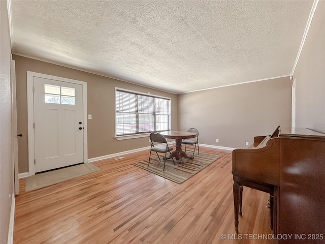 foyer entrance featuring a textured ceiling, crown molding, baseboards, and light wood-style floors