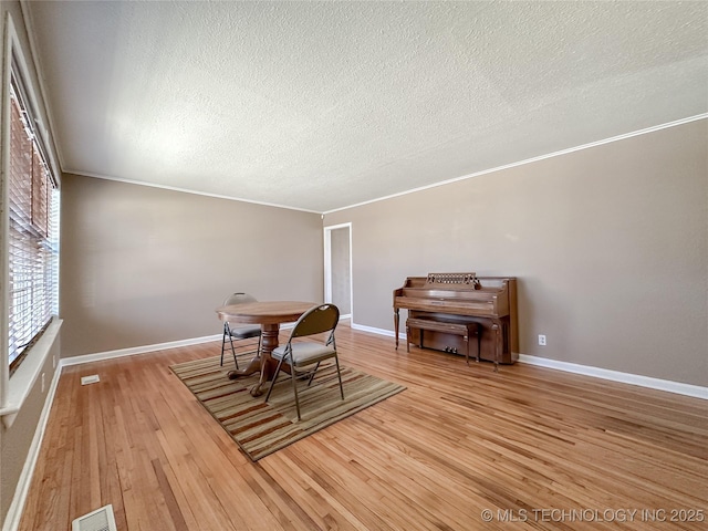 dining area with ornamental molding, wood-type flooring, visible vents, and a textured ceiling