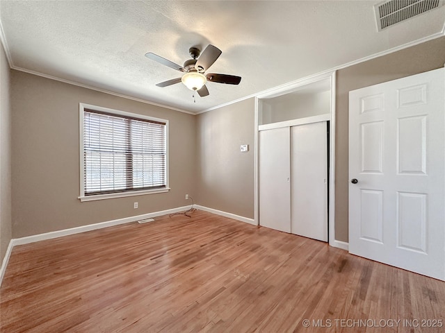 unfurnished bedroom with visible vents, a textured ceiling, crown molding, light wood-type flooring, and a closet