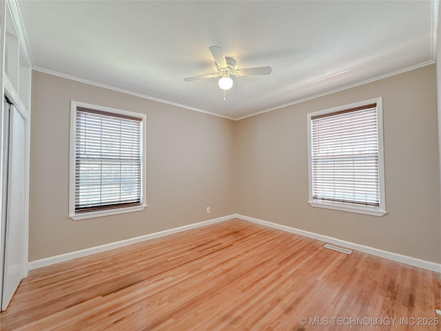 empty room with light wood-type flooring, visible vents, ornamental molding, and baseboards