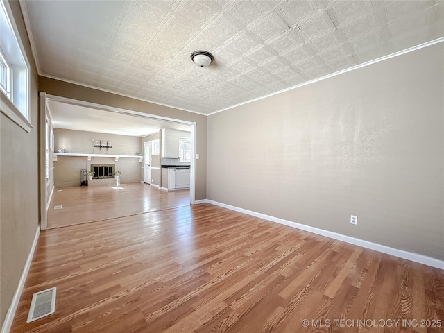 unfurnished living room with light wood finished floors, an ornate ceiling, visible vents, and baseboards