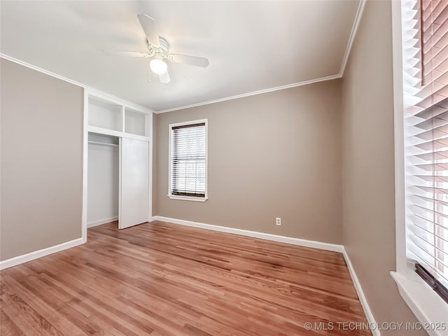 unfurnished bedroom with crown molding, a closet, light wood-style flooring, a ceiling fan, and baseboards