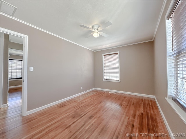 empty room with a ceiling fan, baseboards, visible vents, light wood finished floors, and crown molding