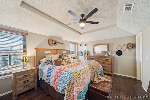 bedroom with a textured ceiling, visible vents, baseboards, dark wood-style floors, and a tray ceiling