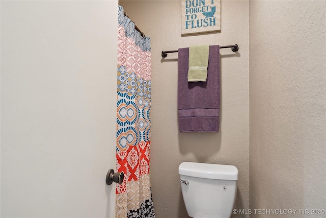 bathroom featuring a textured wall, curtained shower, and toilet