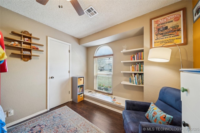 living area featuring a textured ceiling, dark wood-style flooring, visible vents, baseboards, and a ceiling fan