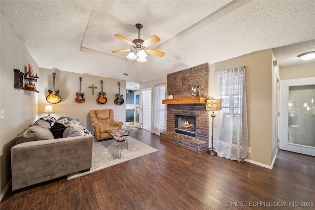 living area with visible vents, ceiling fan, wood finished floors, a tray ceiling, and a fireplace