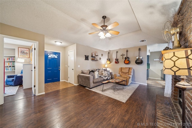 living area with a textured ceiling, ceiling fan, wood finished floors, visible vents, and a tray ceiling