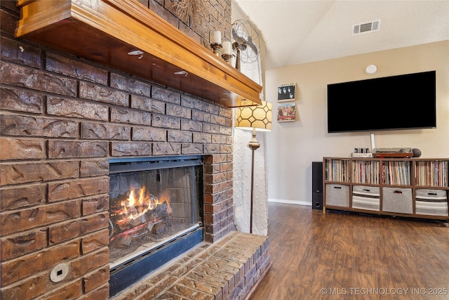 living area with a fireplace, lofted ceiling, visible vents, wood finished floors, and baseboards