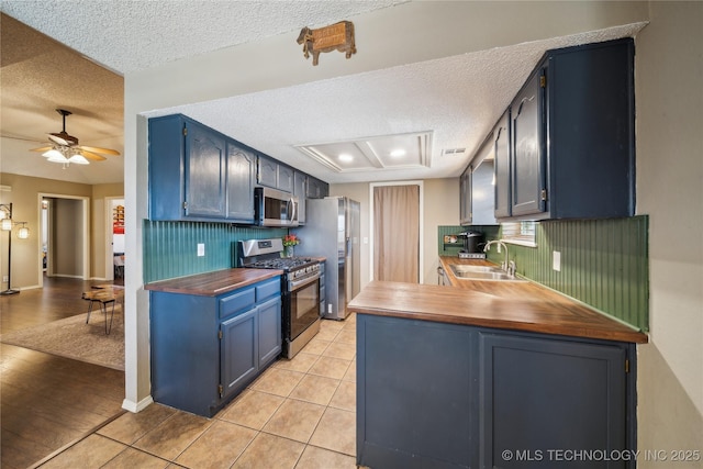 kitchen featuring a textured ceiling, blue cabinets, a sink, appliances with stainless steel finishes, and tasteful backsplash