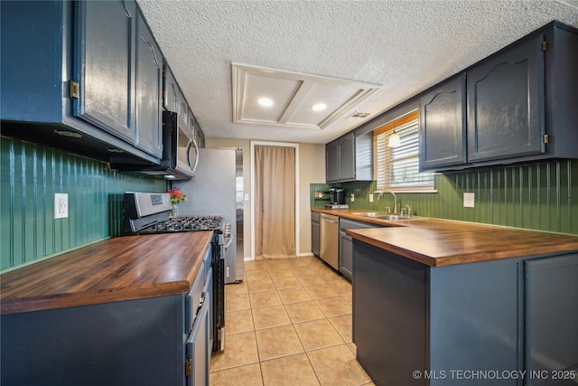 kitchen featuring light tile patterned floors, a textured ceiling, a sink, wooden counters, and appliances with stainless steel finishes