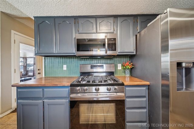 kitchen featuring gray cabinets, a textured ceiling, stainless steel appliances, wooden counters, and light tile patterned flooring