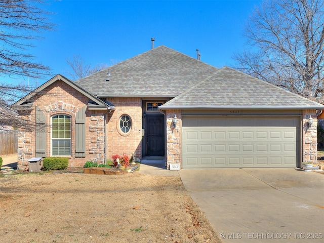 view of front of home featuring roof with shingles, brick siding, an attached garage, stone siding, and driveway