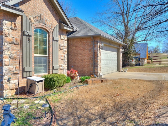 view of property exterior featuring driveway, roof with shingles, a garage, and brick siding