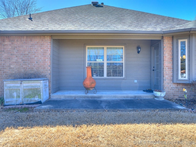 doorway to property with brick siding, roof with shingles, and a porch