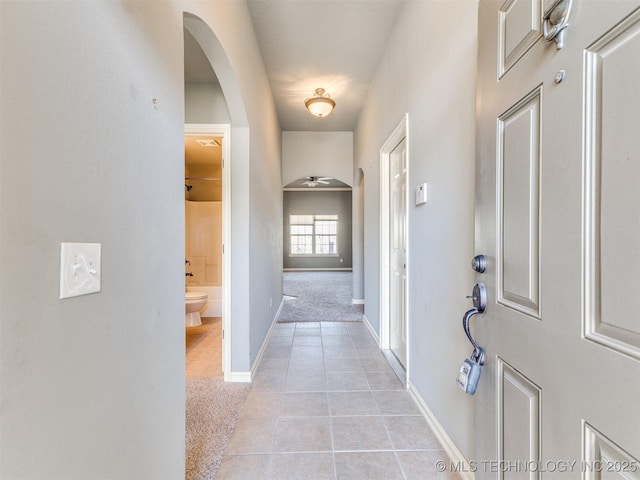 hallway featuring light carpet, light tile patterned floors, baseboards, and arched walkways