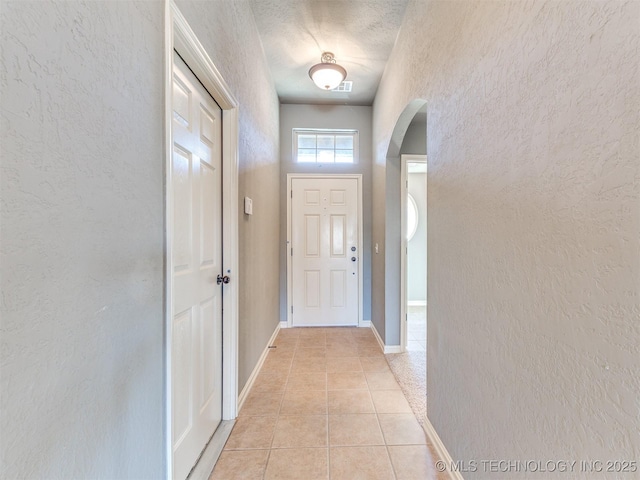 doorway with arched walkways, a textured wall, light tile patterned floors, and baseboards