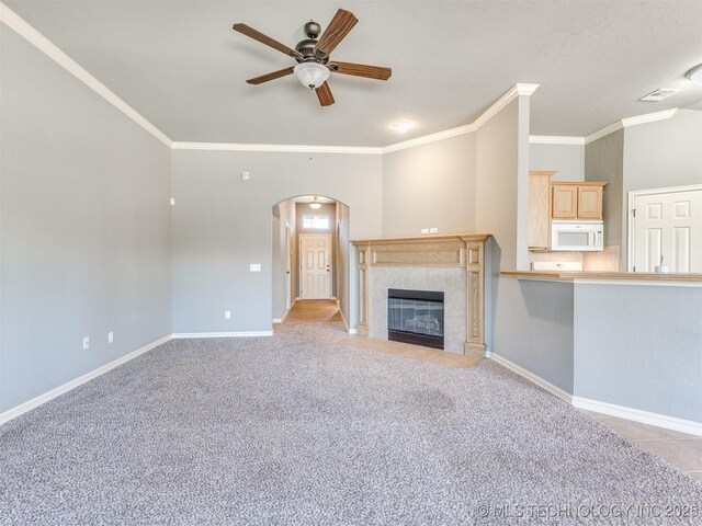 unfurnished living room featuring arched walkways, light carpet, a tile fireplace, and baseboards