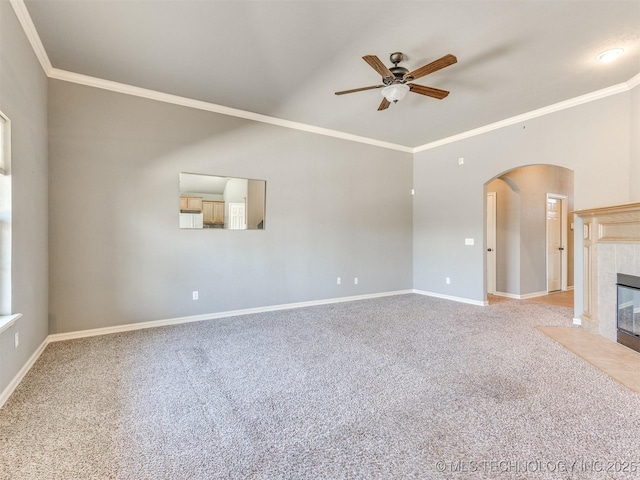 unfurnished living room featuring carpet floors, arched walkways, ornamental molding, a tile fireplace, and baseboards