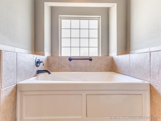 bathroom featuring tile walls, a bath, and wainscoting