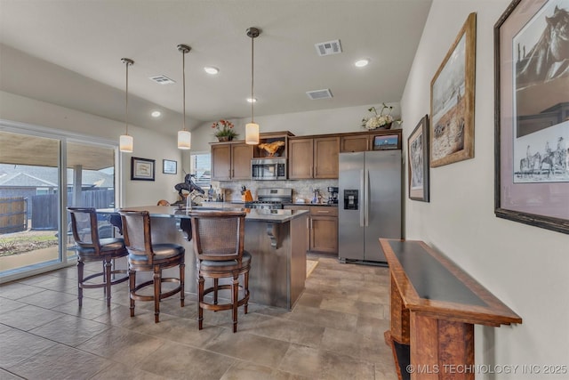 kitchen with a breakfast bar area, stainless steel appliances, visible vents, decorative backsplash, and a center island with sink