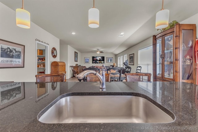 kitchen featuring dark stone counters, pendant lighting, a sink, and ceiling fan