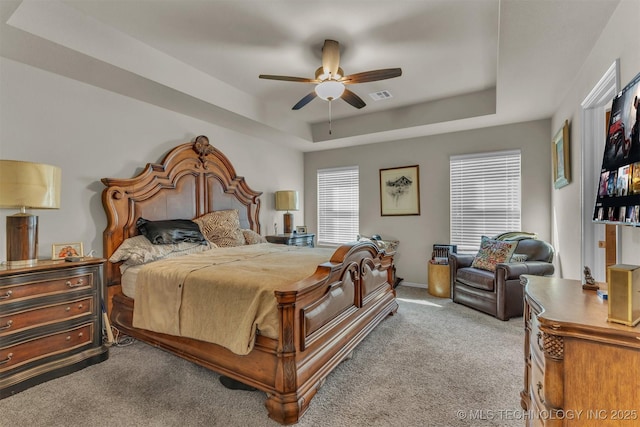 carpeted bedroom featuring baseboards, a tray ceiling, visible vents, and a ceiling fan