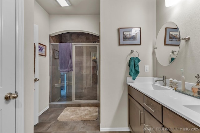 bathroom featuring baseboards, double vanity, a sink, and a shower stall