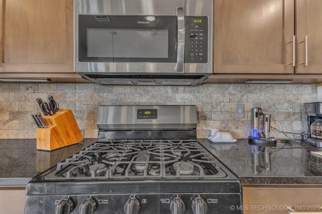 kitchen with appliances with stainless steel finishes, dark stone counters, and tasteful backsplash