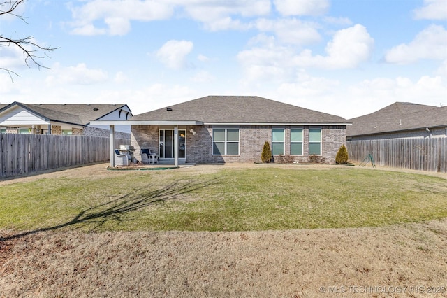 rear view of house with brick siding, a yard, a fenced backyard, and roof with shingles