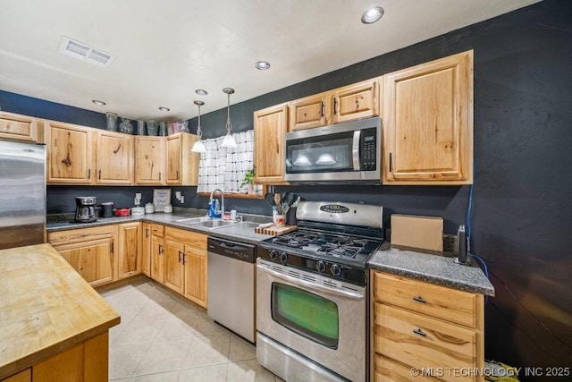 kitchen featuring light tile patterned flooring, a sink, visible vents, hanging light fixtures, and appliances with stainless steel finishes