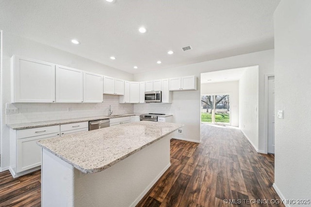 kitchen with dark wood finished floors, decorative backsplash, stainless steel appliances, a sink, and a center island
