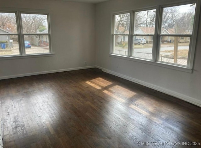 empty room featuring a healthy amount of sunlight, dark wood finished floors, and baseboards