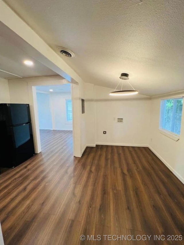 empty room with a textured ceiling, dark wood finished floors, visible vents, and baseboards