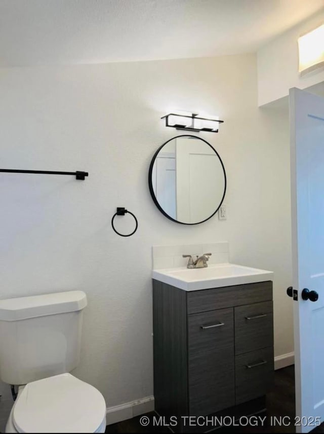 half bath featuring baseboards, vanity, and toilet